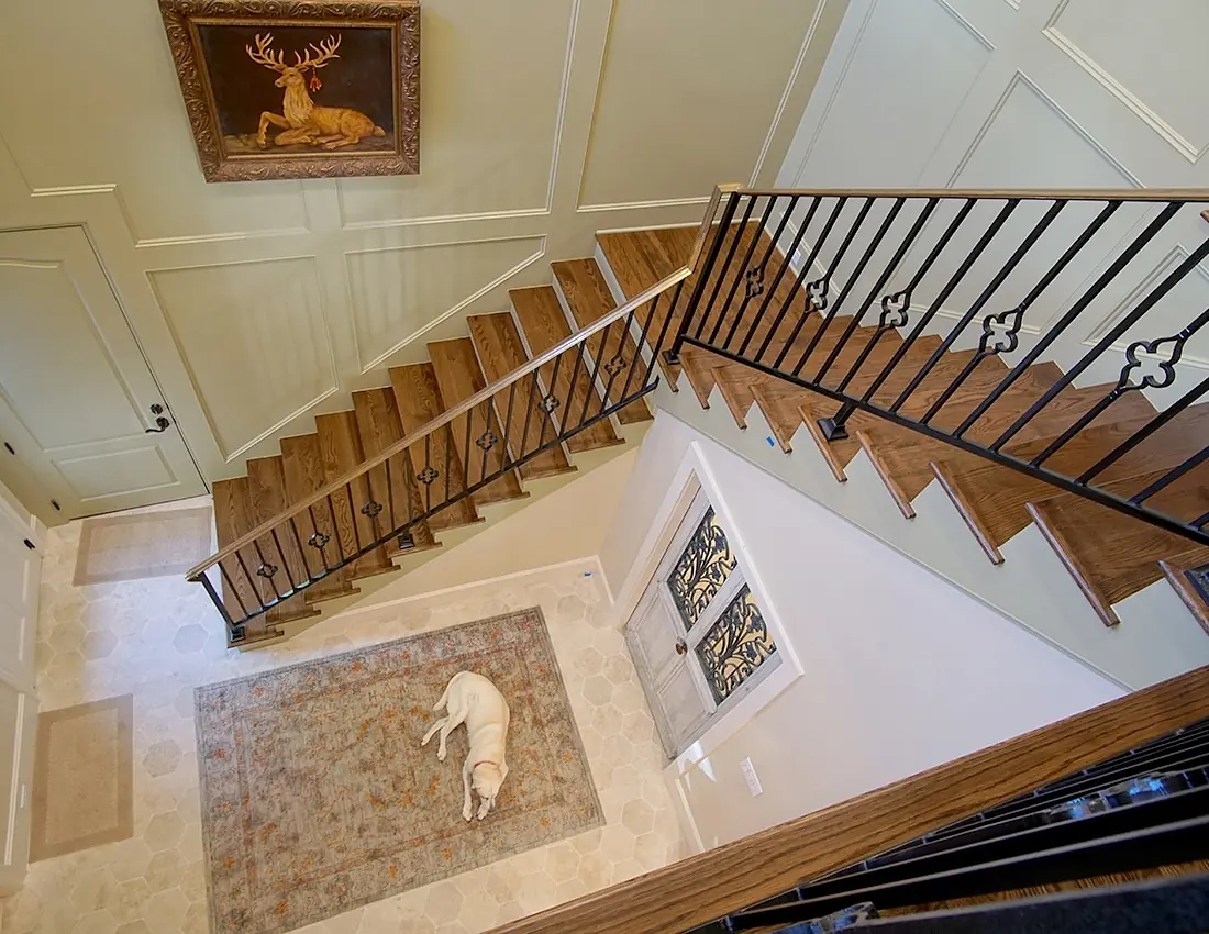 Foyer with area rug, ornate staircase, framed artwork, and dog on the rug.