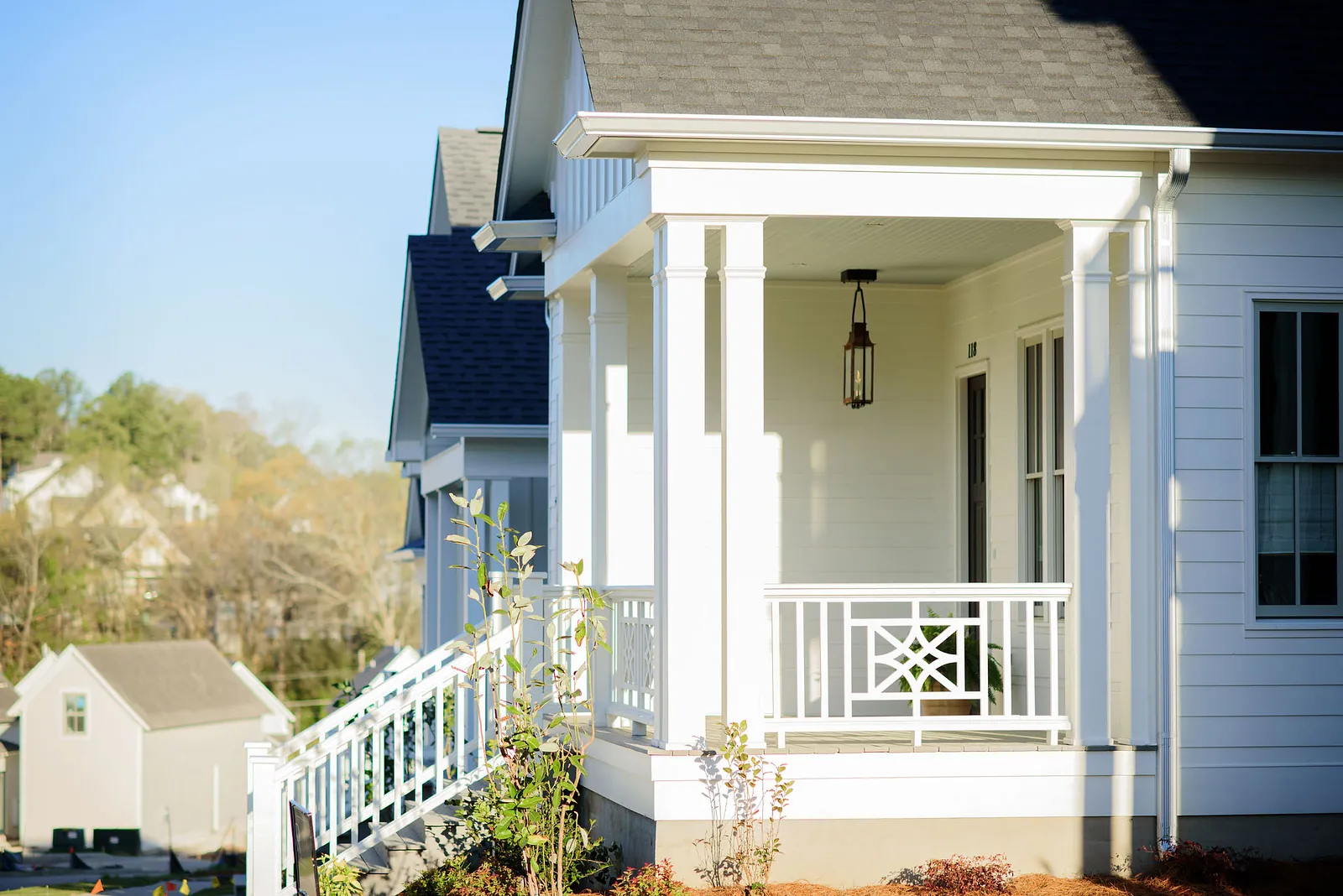 Exterior front view of a house with white siding, porch, railings, hanging lantern, and landscaping.