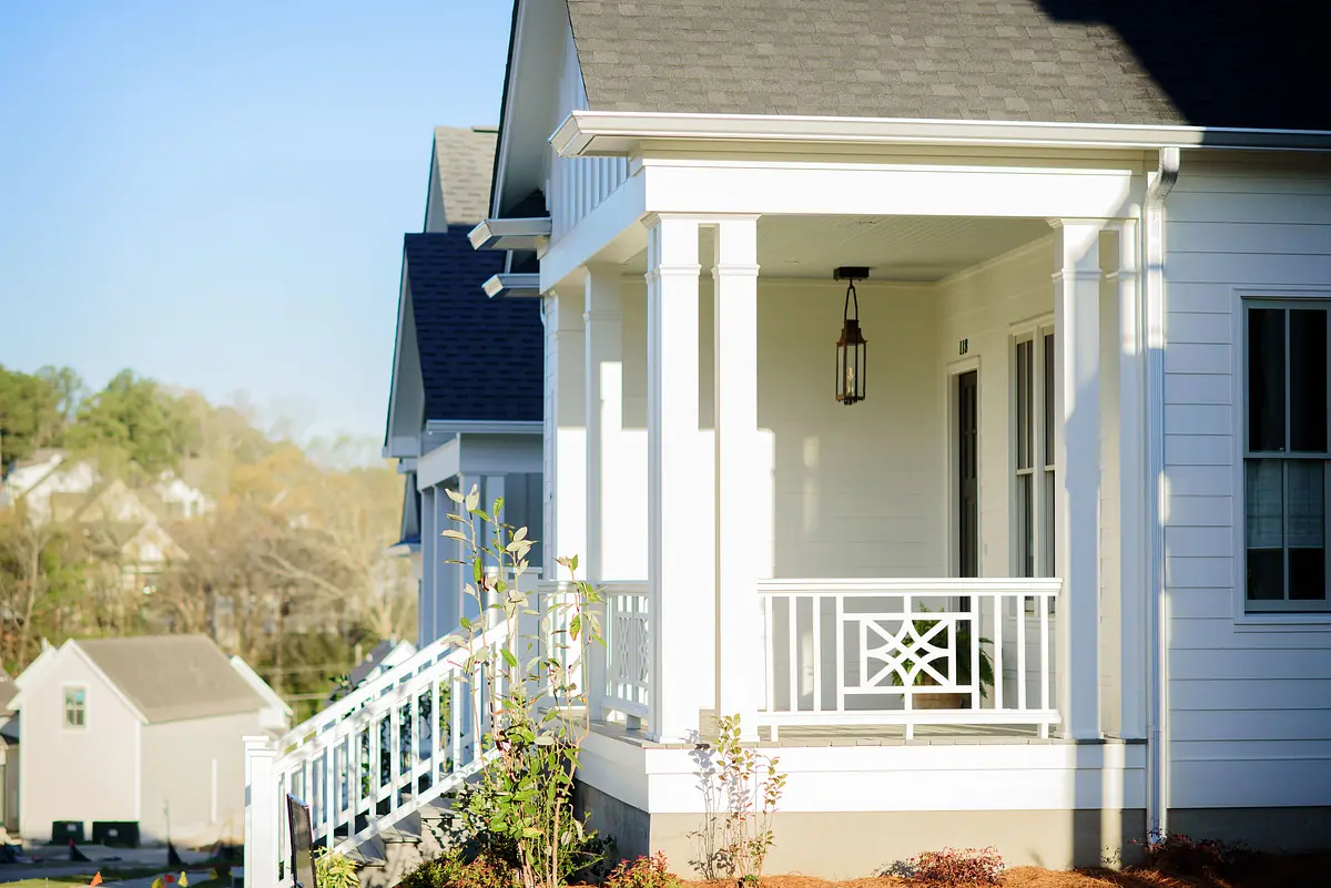 Exterior front view of a house with white siding, porch, railings, hanging lantern, and landscaping.