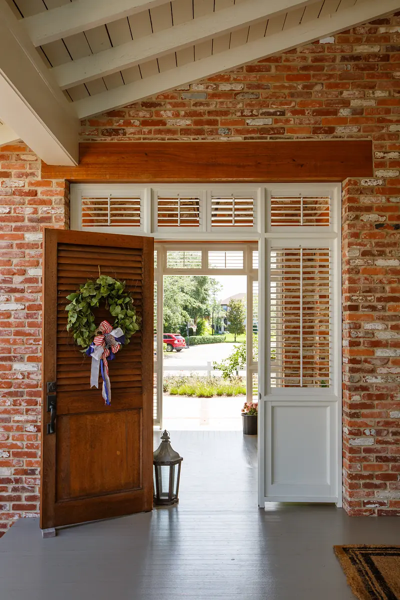 Foyer with wooden door, brick walls, shutters, and a floor lantern.