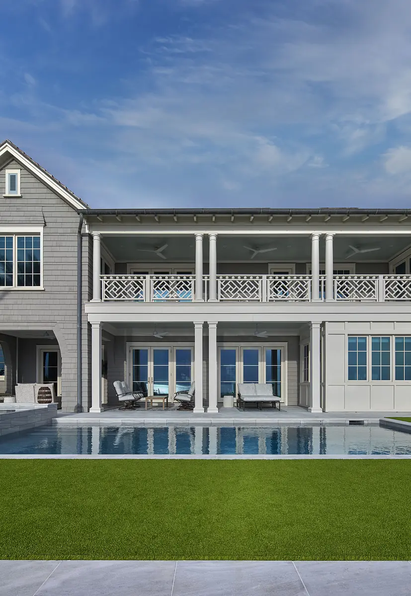 Exterior rear view with swimming pool, patio, lounge chairs, and a house with large windows and balcony.