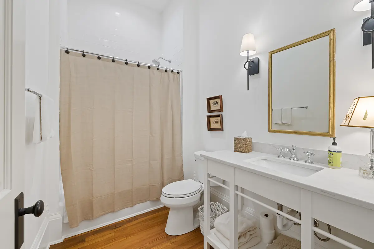 Bathroom with white vanity, marble countertop, beige shower curtain, and white toilet.