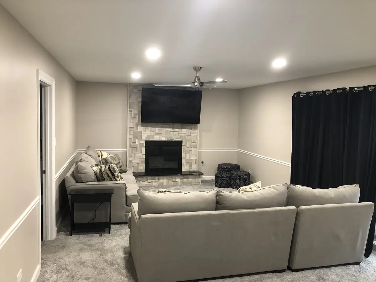 Living room with gray sectional sofa, black side table, television, stone fireplace, and black curtains.