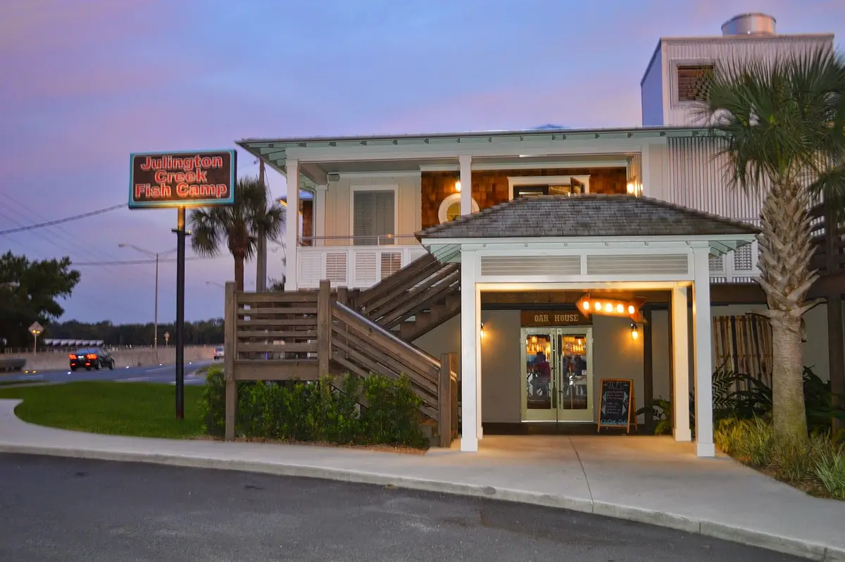 Exterior front view of a building with a porch, steps, palm trees, and a second-level balcony.
