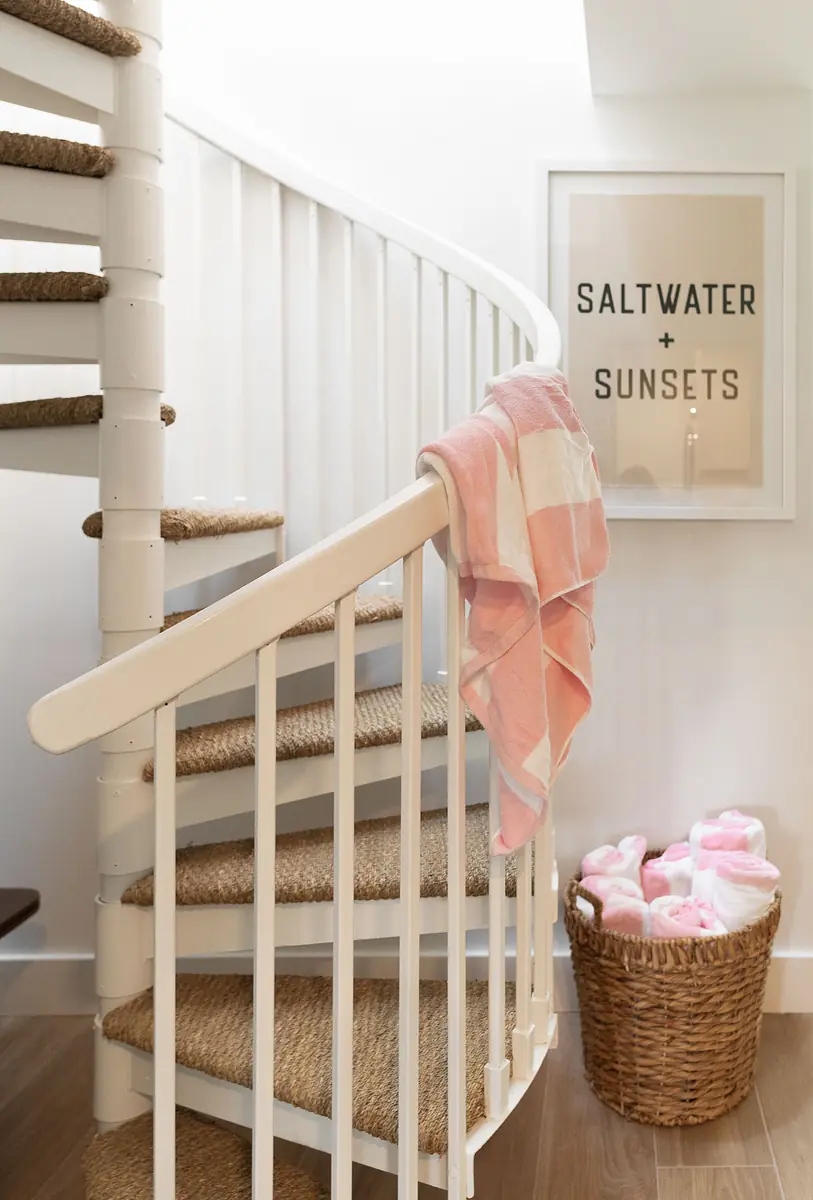 Spiral staircase with pink striped towel, framed poster, and wicker basket at the base.