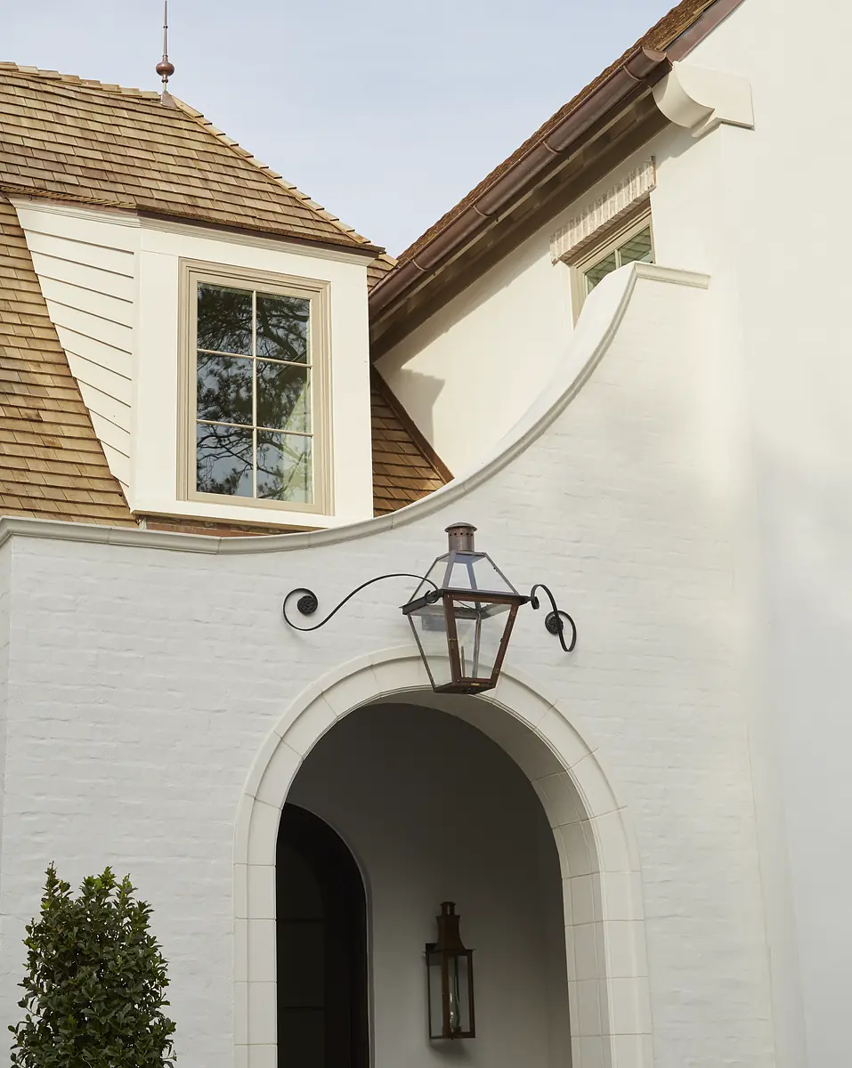 Exterior front with white brick archway, large window, shingled roof, and decorative wall sconces.