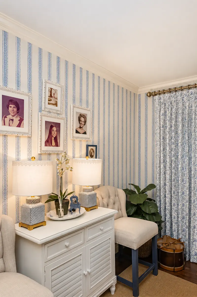Small room with tufted armchair, console table, patterned wallpaper, table lamps, and potted plant.