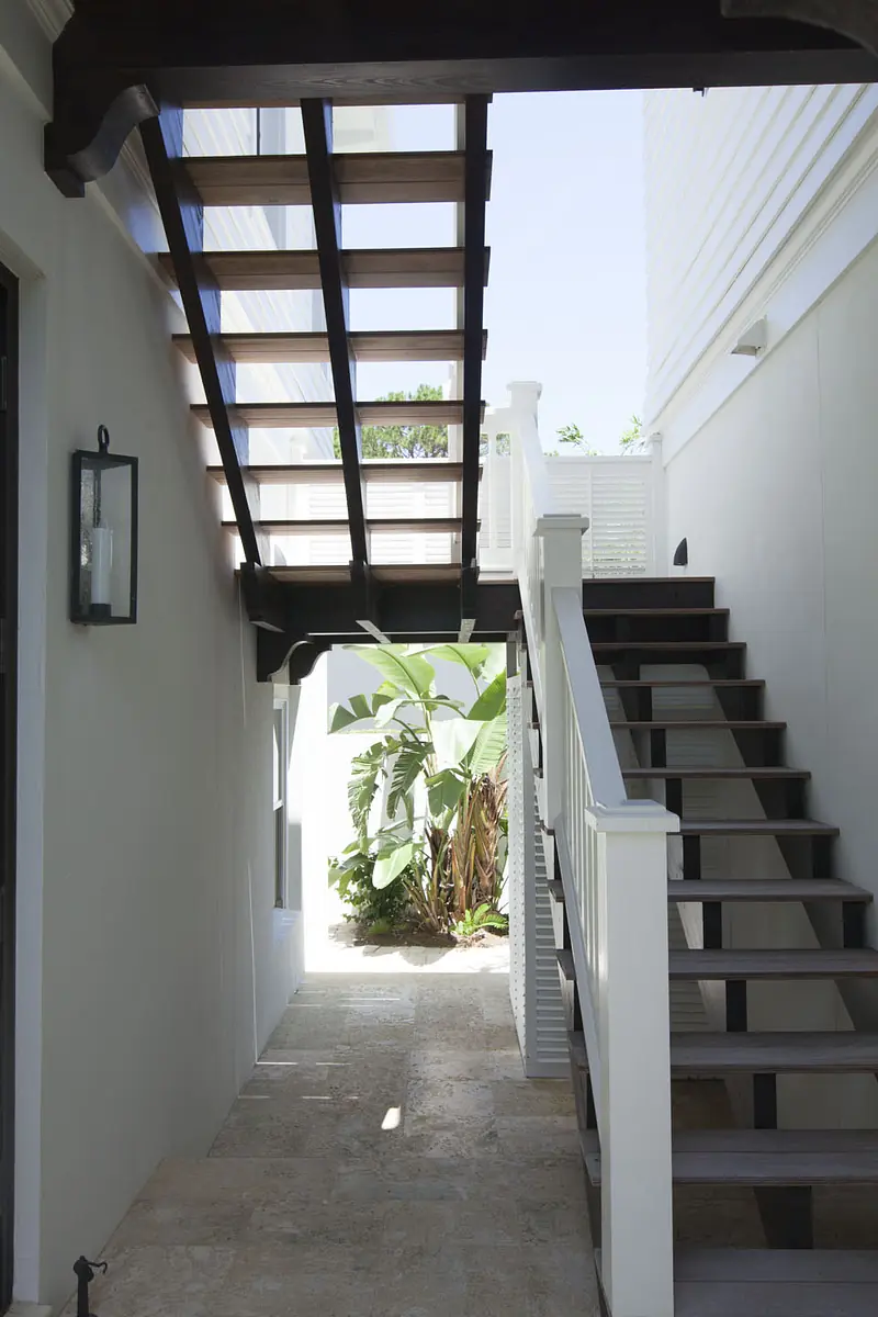 Hallway with wooden staircase, white railing, stone floor, and large windows leading to a garden area