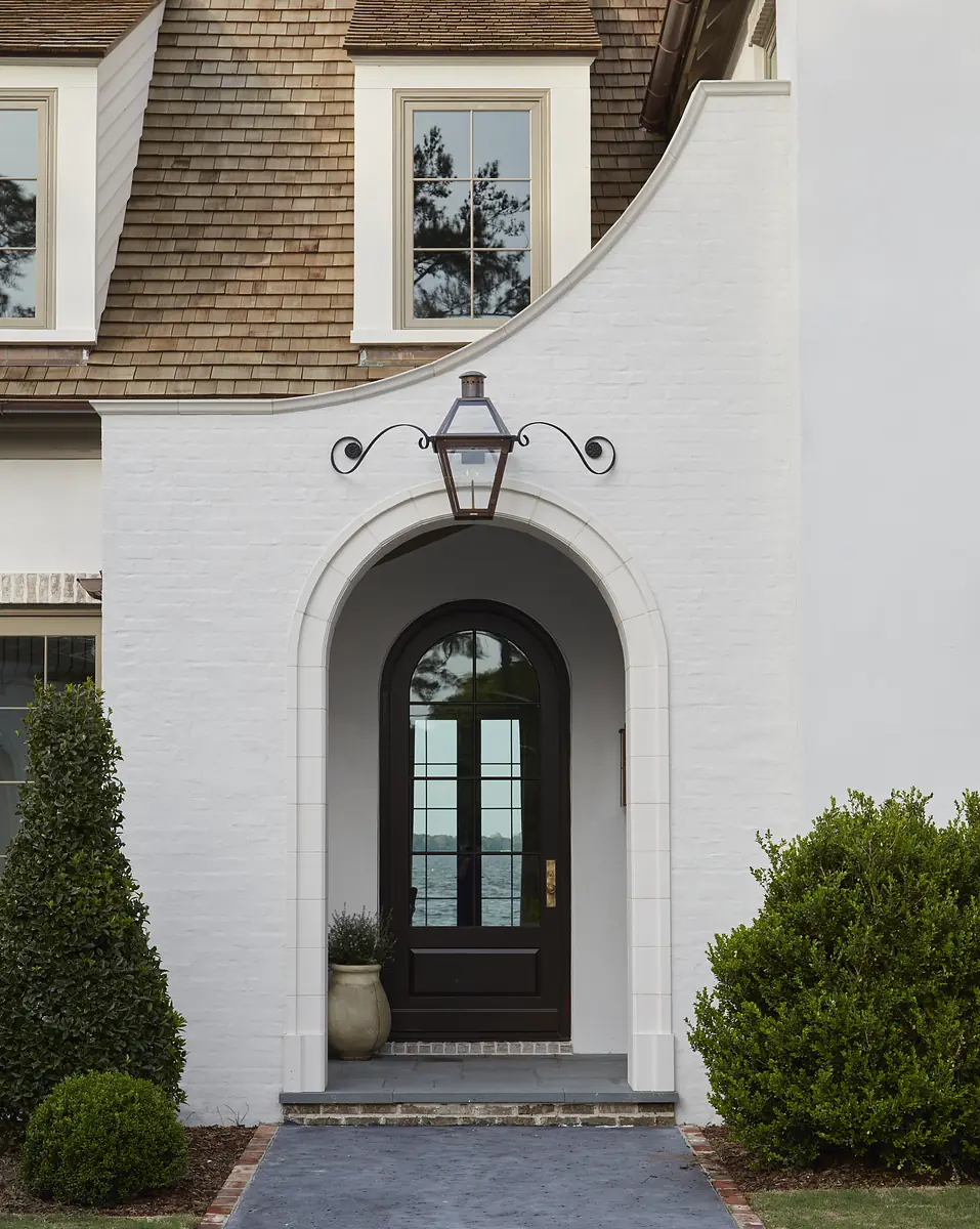 Exterior entrance with arched doorway, dark door, white walls, manicured shrubs, and grey stone path.