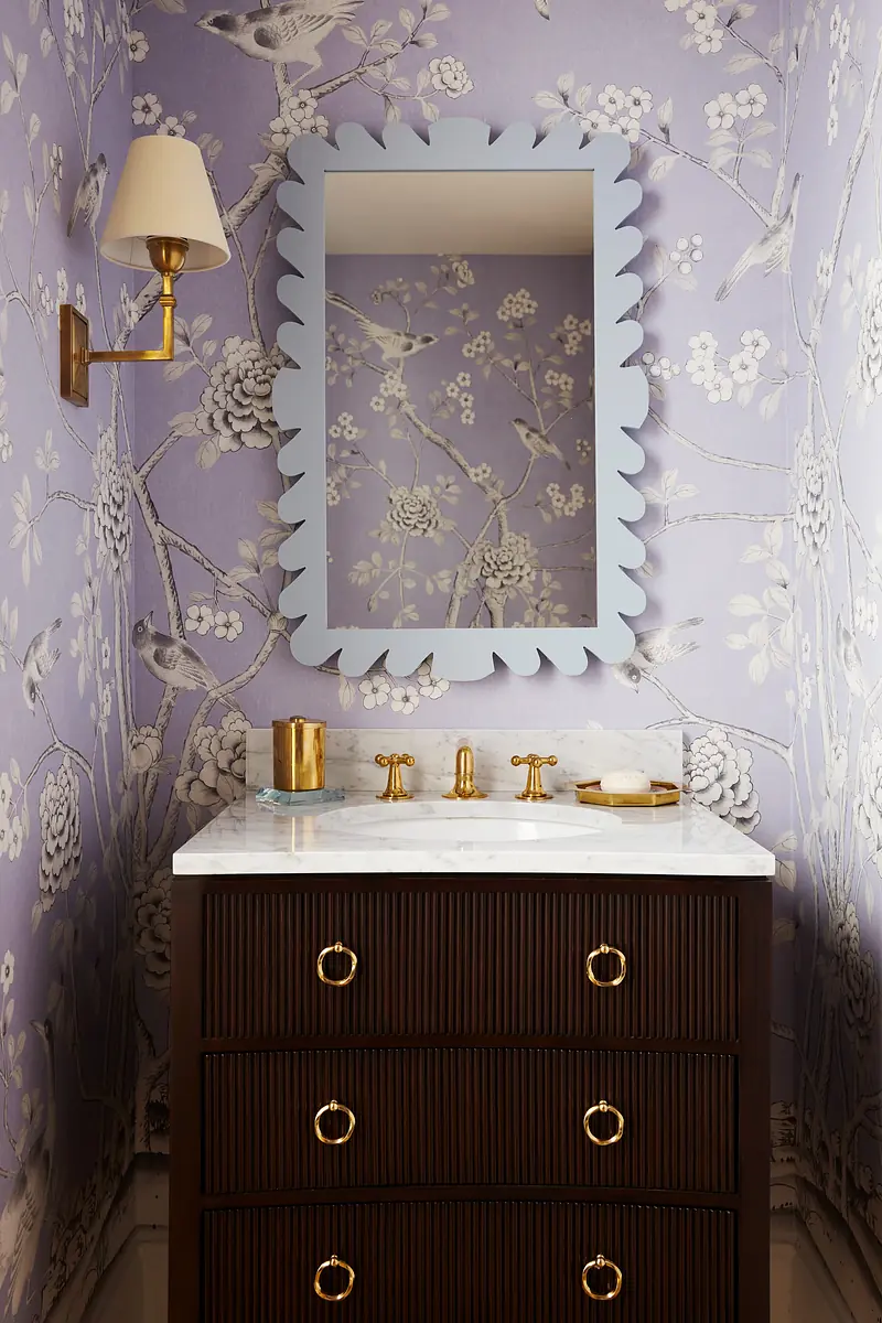 Bathroom with dark wood vanity, marble countertop, floral wallpaper, and wall sconce.