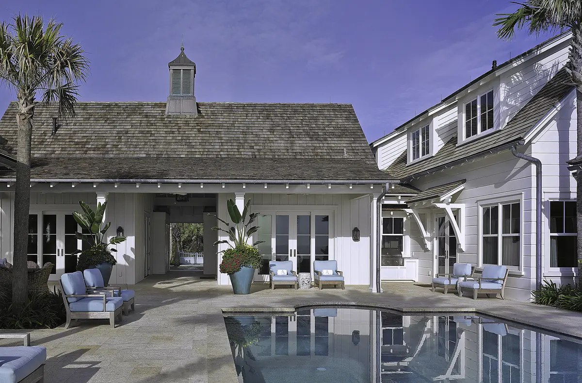 Exterior rear area with swimming pool, blue lounge chairs, planters, and white house with gabled roof.