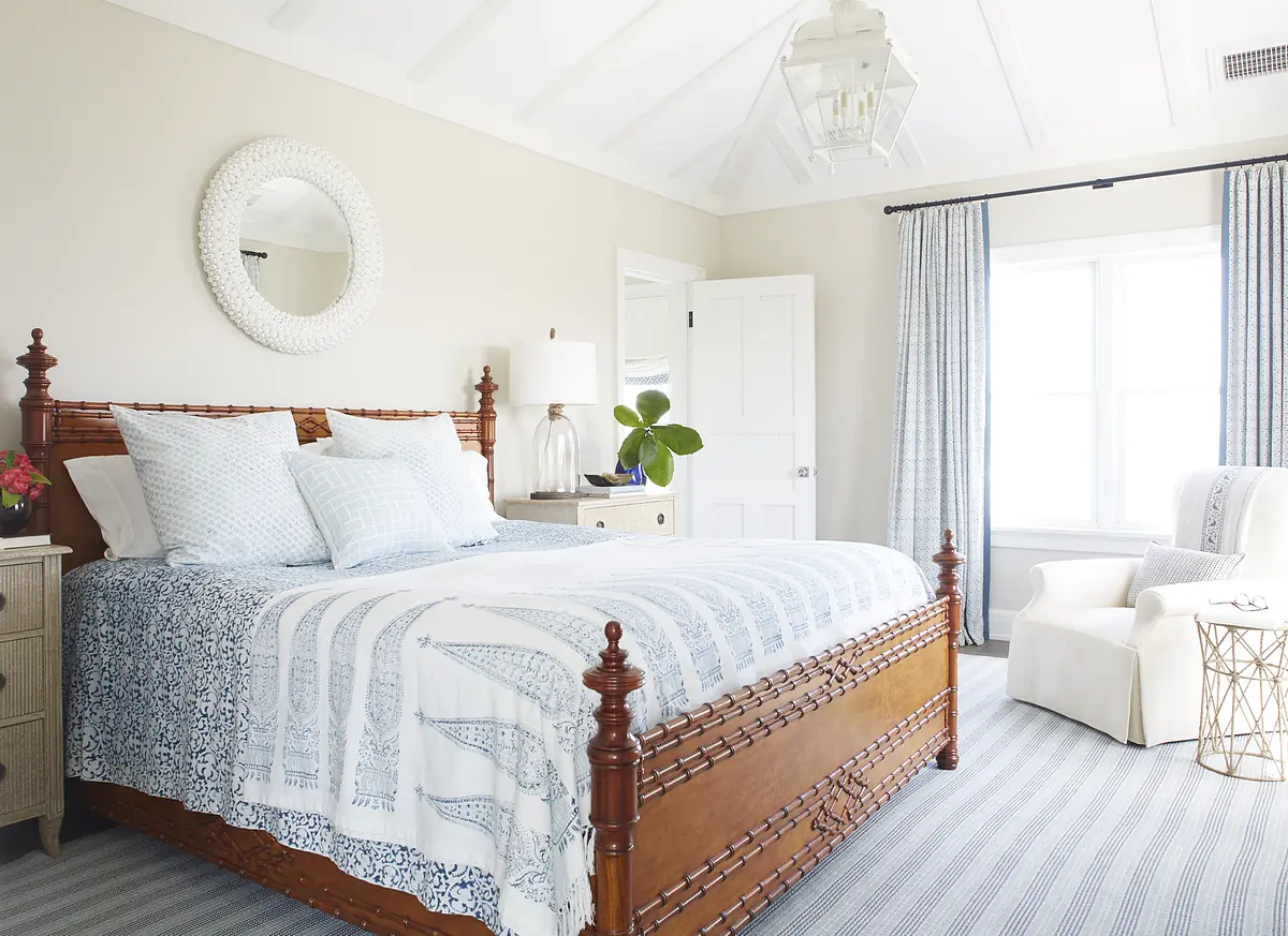 Bedroom with wooden bed, blue bedding, nightstand, lamp, chair, and striped rug with natural light from window