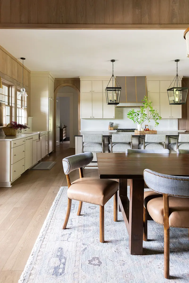 Dining room with wooden table, leather chairs, patterned rug, and pendant lights.