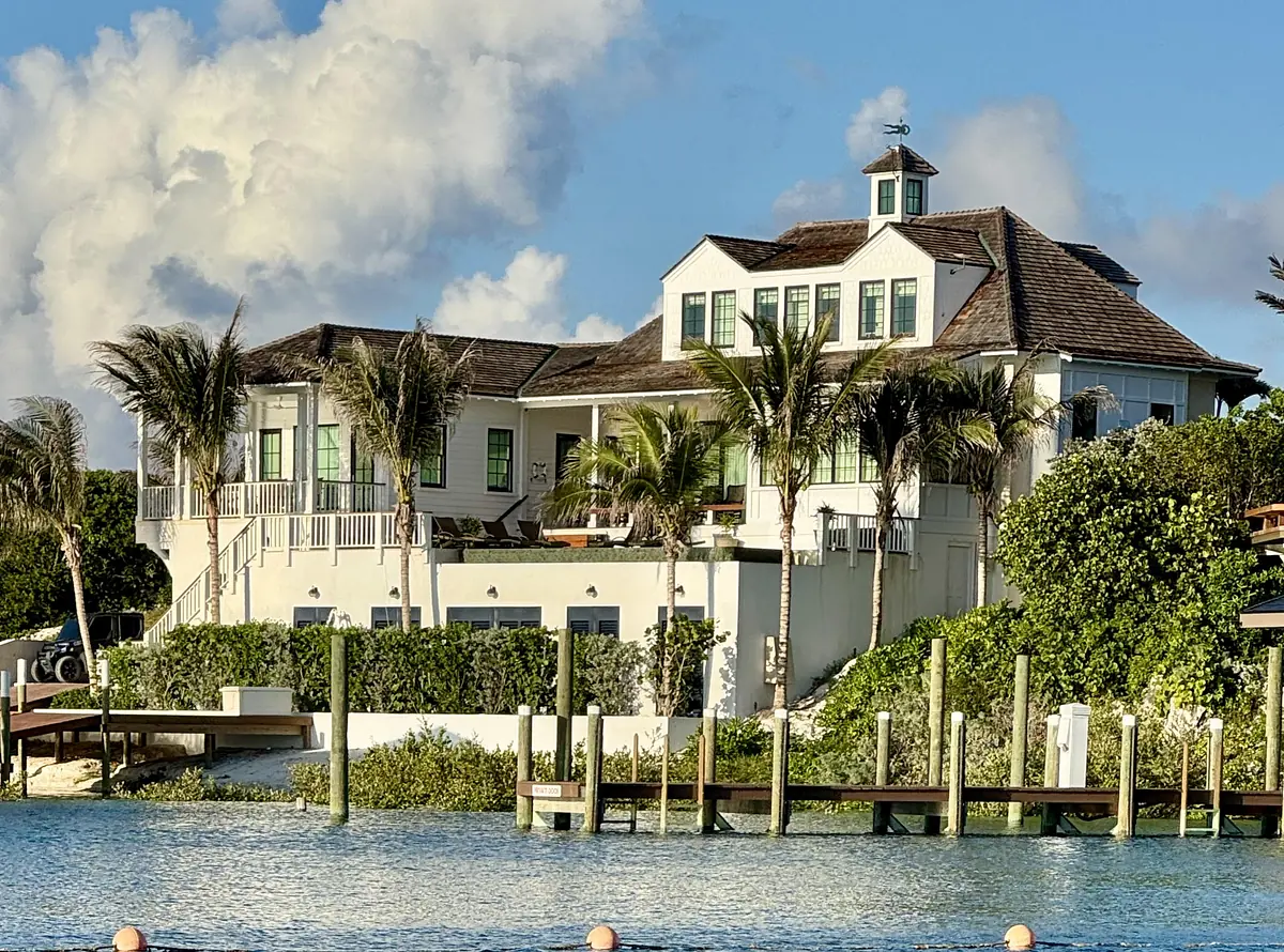 Two-story house with white and gray exterior, green shutters, wraparound porch, and palm trees.