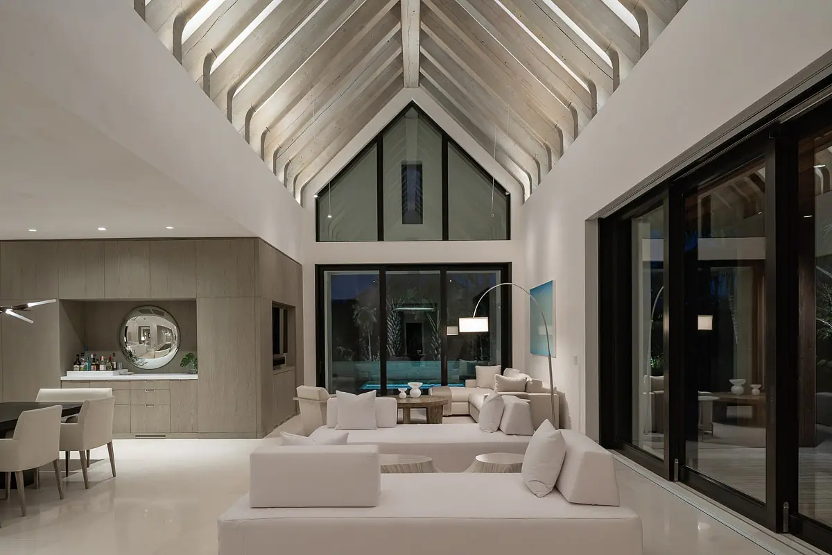 Living room with white sectional sofa, coffee table, armchairs, large glass doors, and exposed wooden beams.