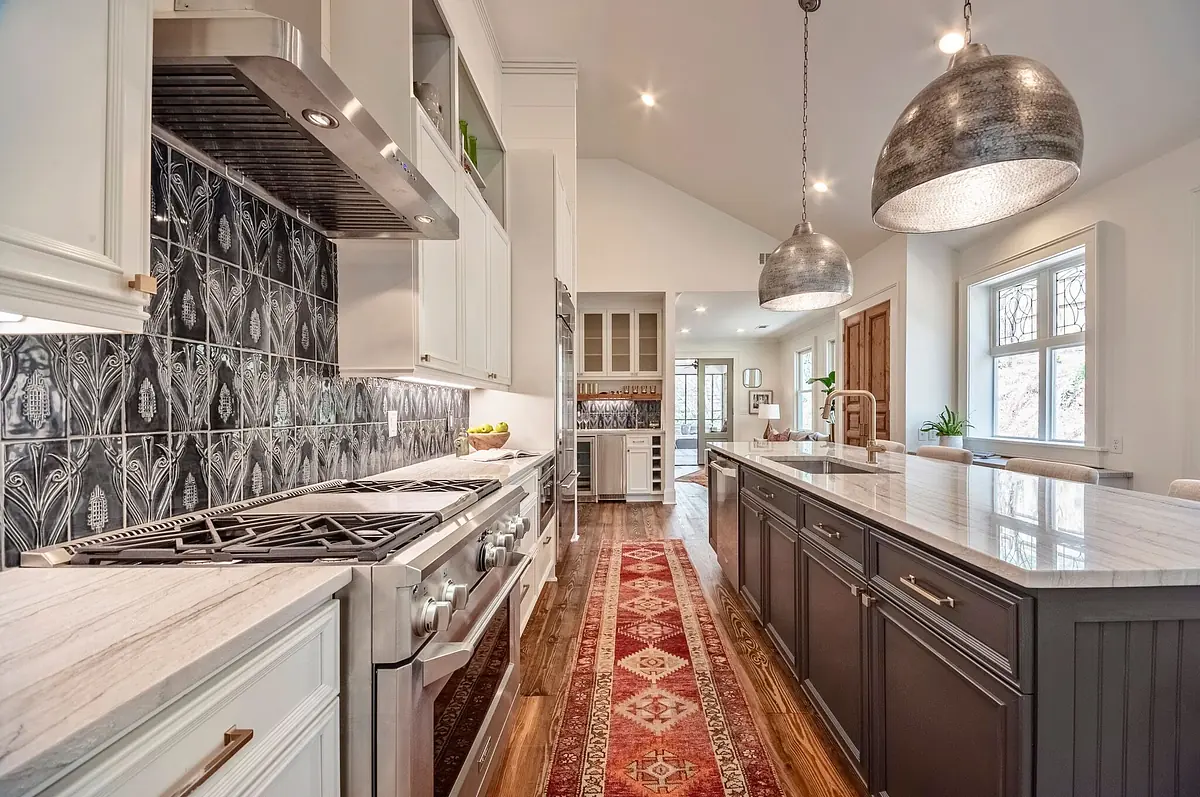 Kitchen with gas range, dark gray island, marble countertop, patterned backsplash, and wooden cabinets.