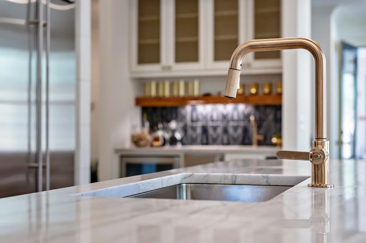 Kitchen with marble countertop, undermount sink, brass faucet, and wooden shelves above glass cabinets.
