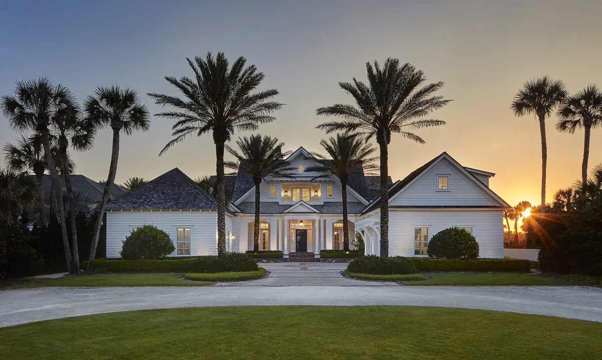 Exterior front view of a house with gabled roofs, palm trees, and a central entryway