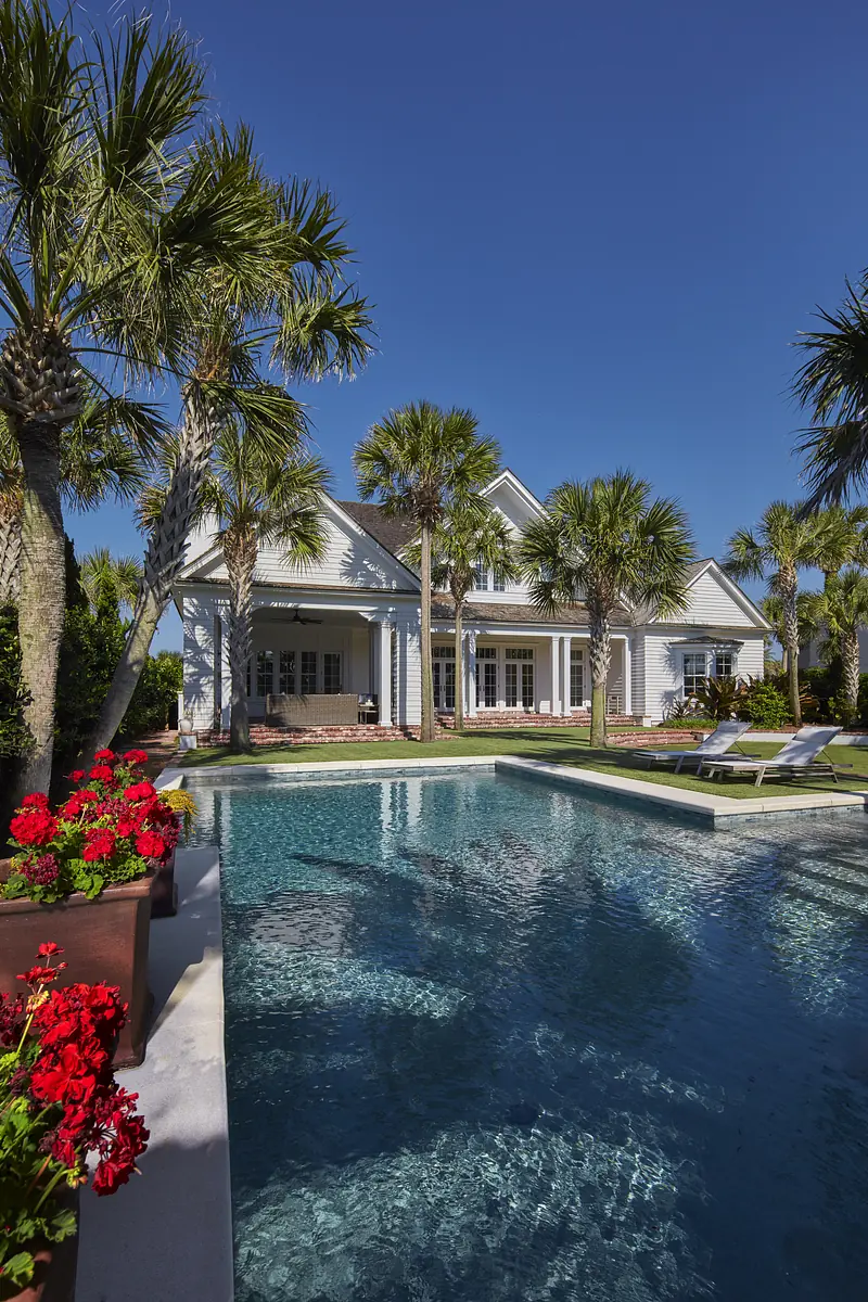 Exterior view with swimming pool, palm trees, landscaped area, and lounge chairs beside the pool