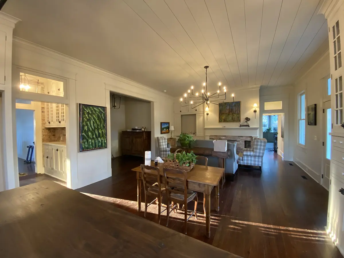 Dining room with wooden table, six chairs, paintings on walls, sideboard, and chandelier.