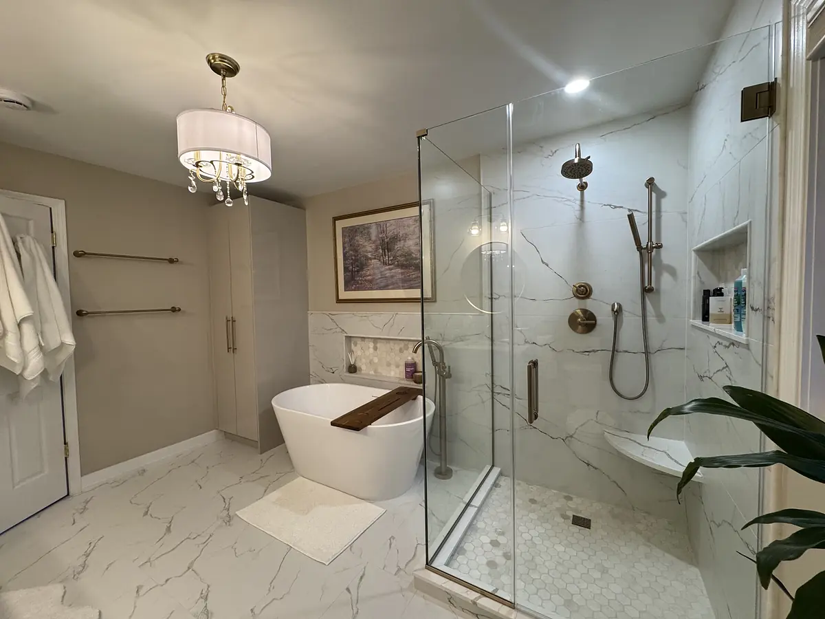Bathroom with freestanding tub, glass shower, marble tiles, vanity, towel rack, and a plant.