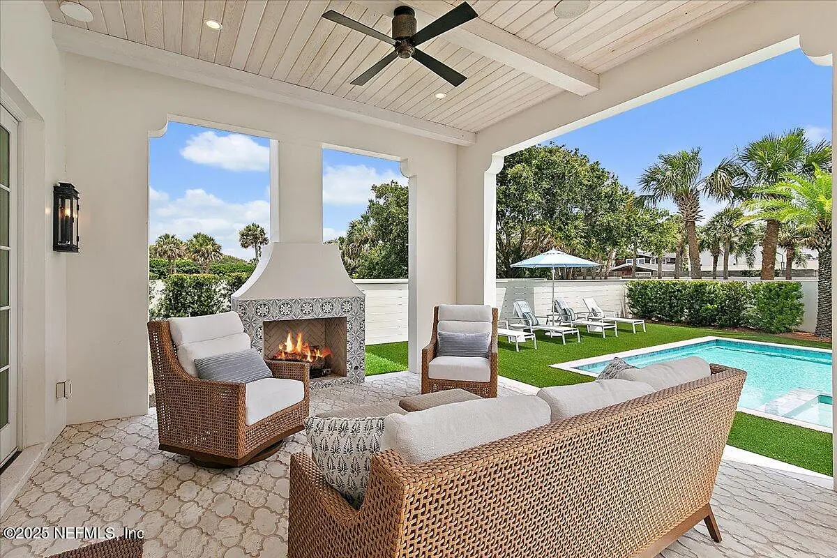 Patio with wicker seating, coffee table, stone fireplace, swimming pool, and palm trees.