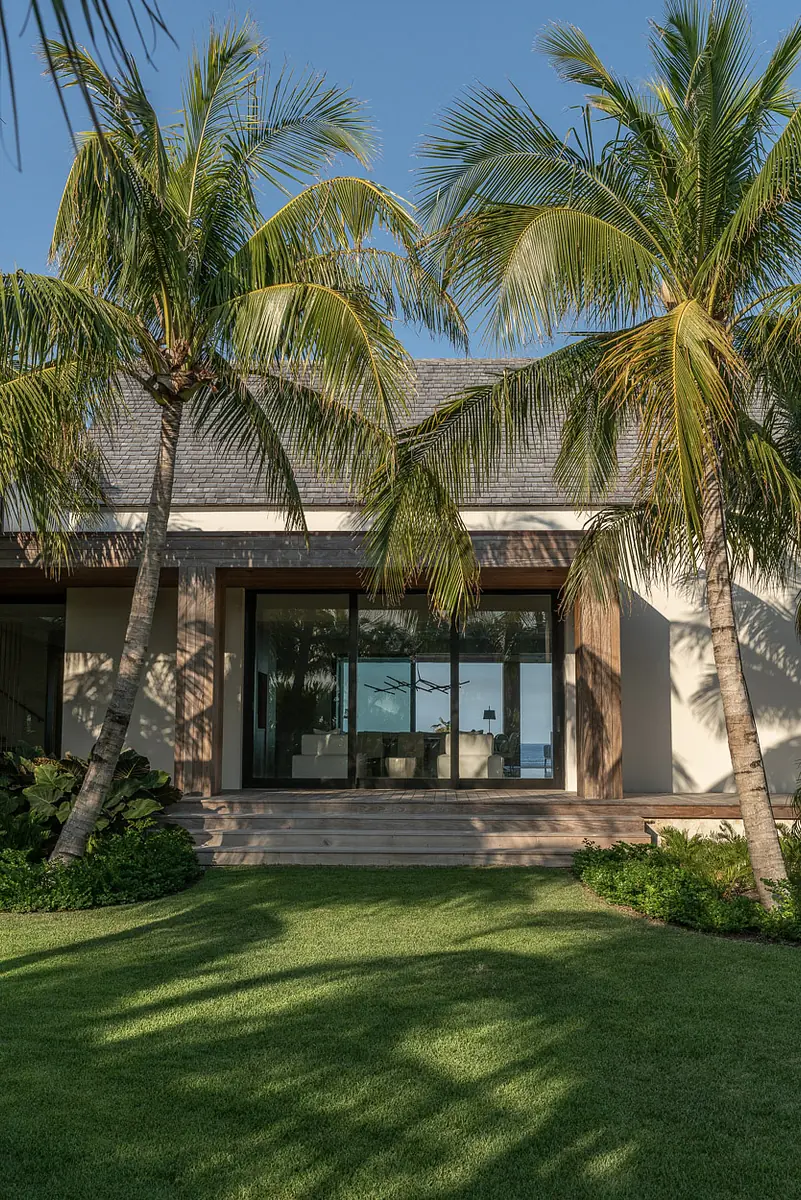 Exterior front view of a modern house with sliding doors, palm trees, and well-maintained lawn.