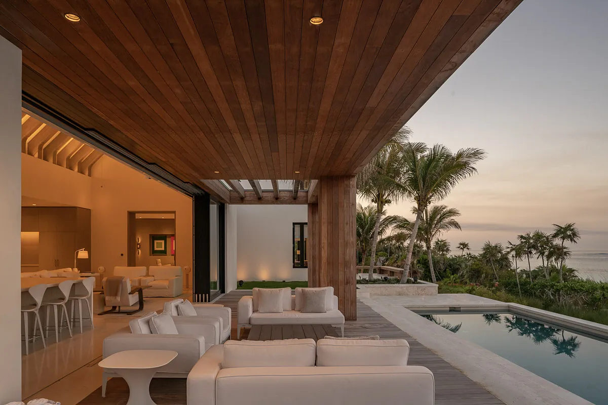 Patio with white sofas, side table, pool view, and wooden ceiling under evening sky