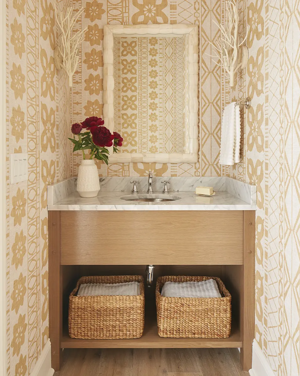 Powder room with wall-mounted sink, marble top, light wood cabinet, and patterned gold and white wallpaper.