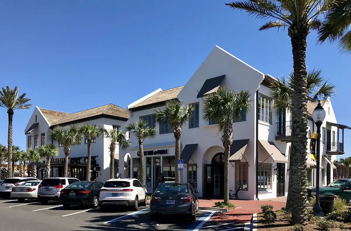 Commercial building with white walls, thatched roof, palm trees, and cars in front.
