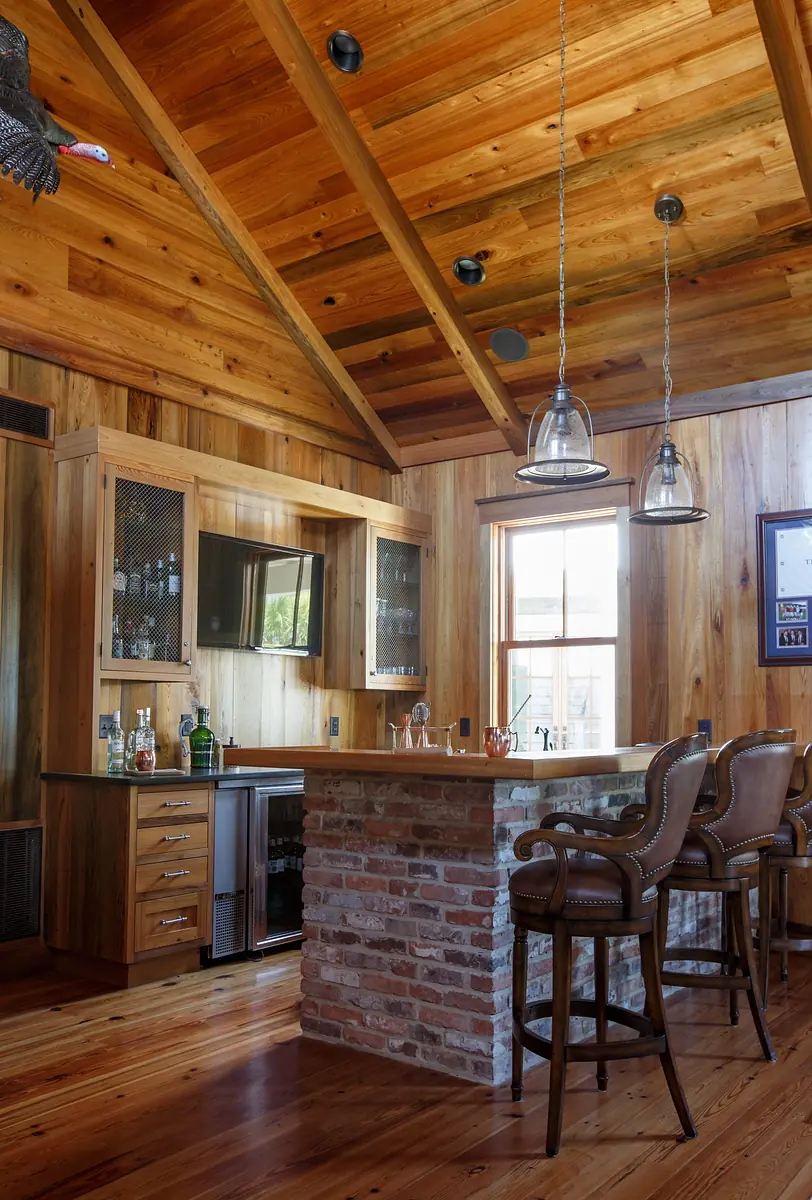 Room with bar area, wooden counter, bar stools, cabinets, and exposed beam ceiling with pendant lights