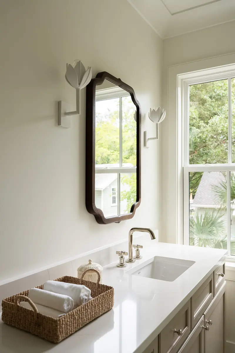 Bathroom with sink, decorative mirror, wall-mounted fixtures, and basket of rolled towels.