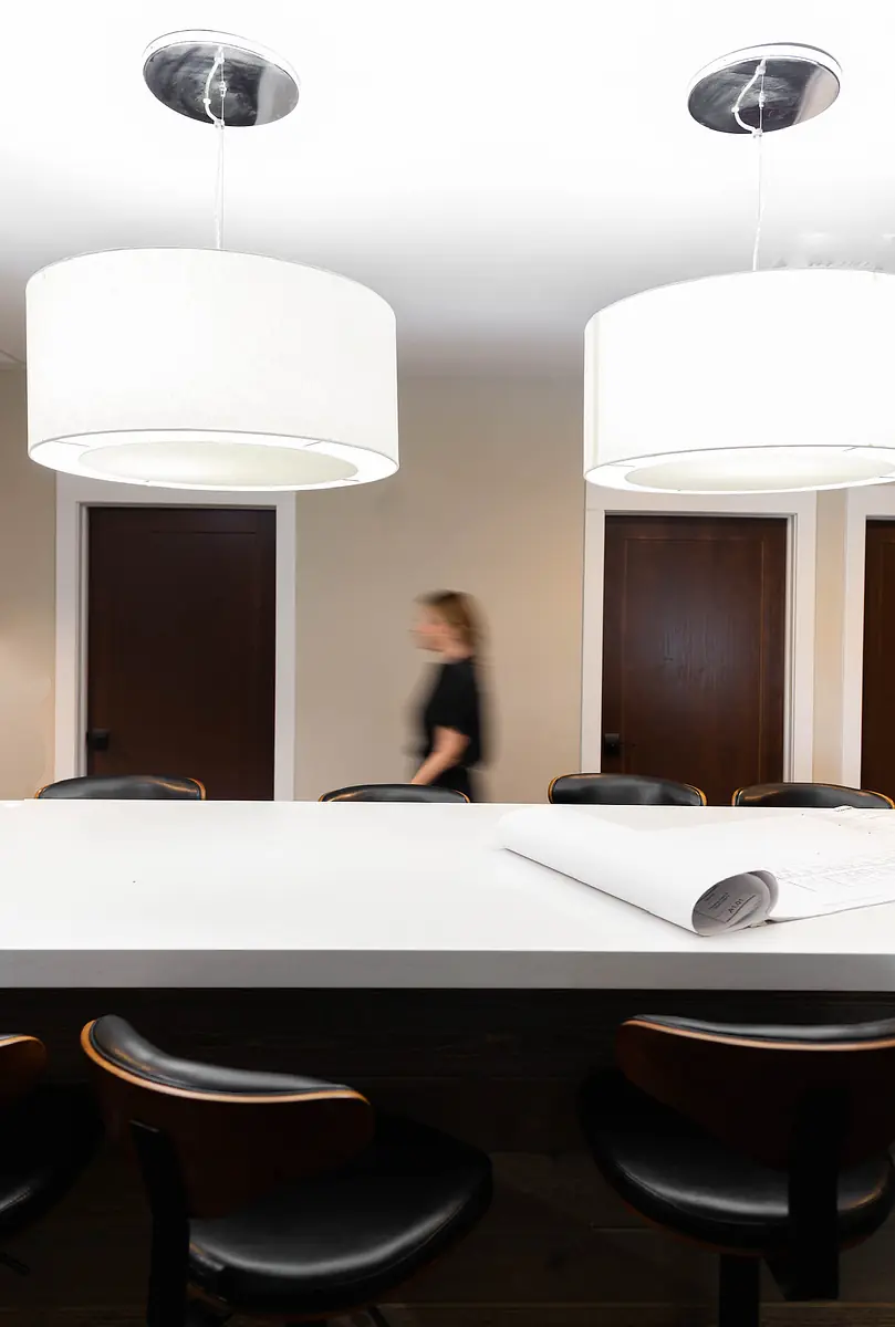 Open space with white countertop, black chairs, two doors, and pendant lights above.
