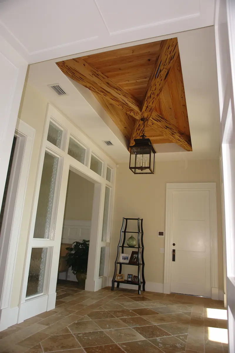 Foyer with wooden beam ceiling, lantern light, decorative rack, stone tile floor, and frosted glass doors.