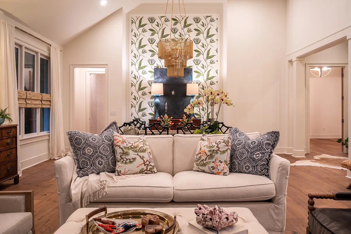 Living room with white sofa, floral wallpaper, artwork, coffee table, and natural light from large windows.