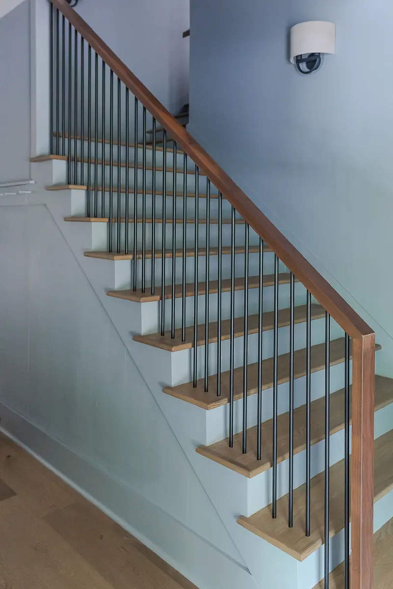 Hallway with staircase, wooden treads, metal balusters, wall sconce, and wood flooring.