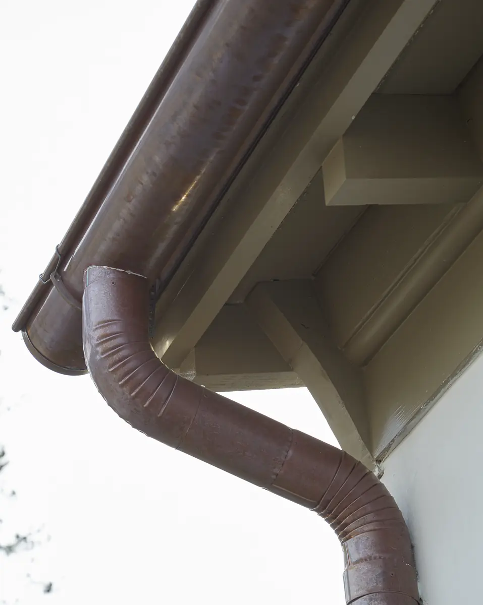 Exterior front showing brown metal gutter and downspout attached to light-colored wall.