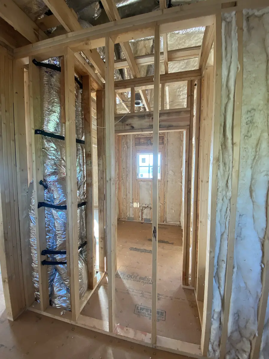 Unfinished space with exposed wooden framing, insulation, and a window opening.