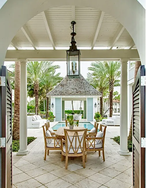 Patio with round wood dining table, six wooden chairs, swimming pool, palm trees, and gazebo structure
