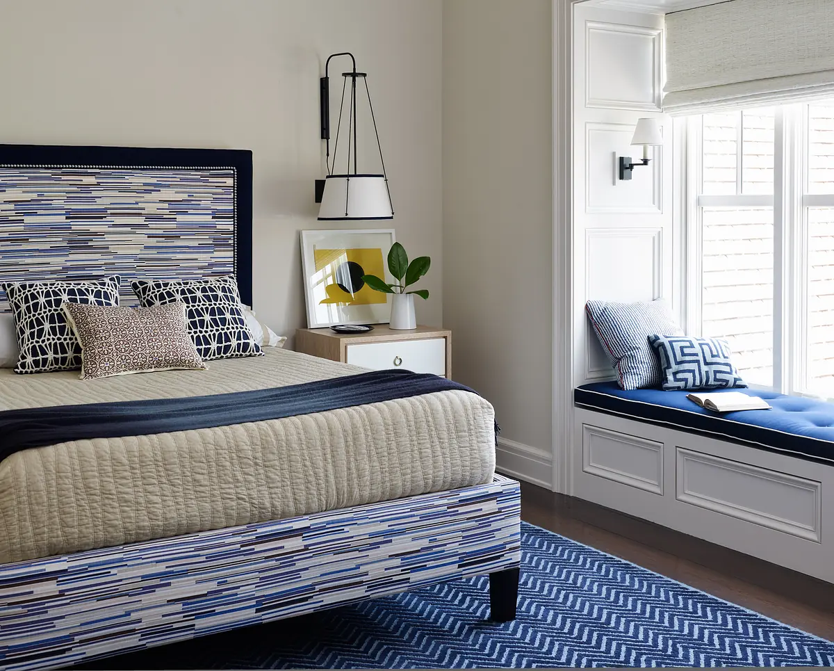 Bedroom with patterned bed, bedside table, window seat, rug, and geometric pillows.