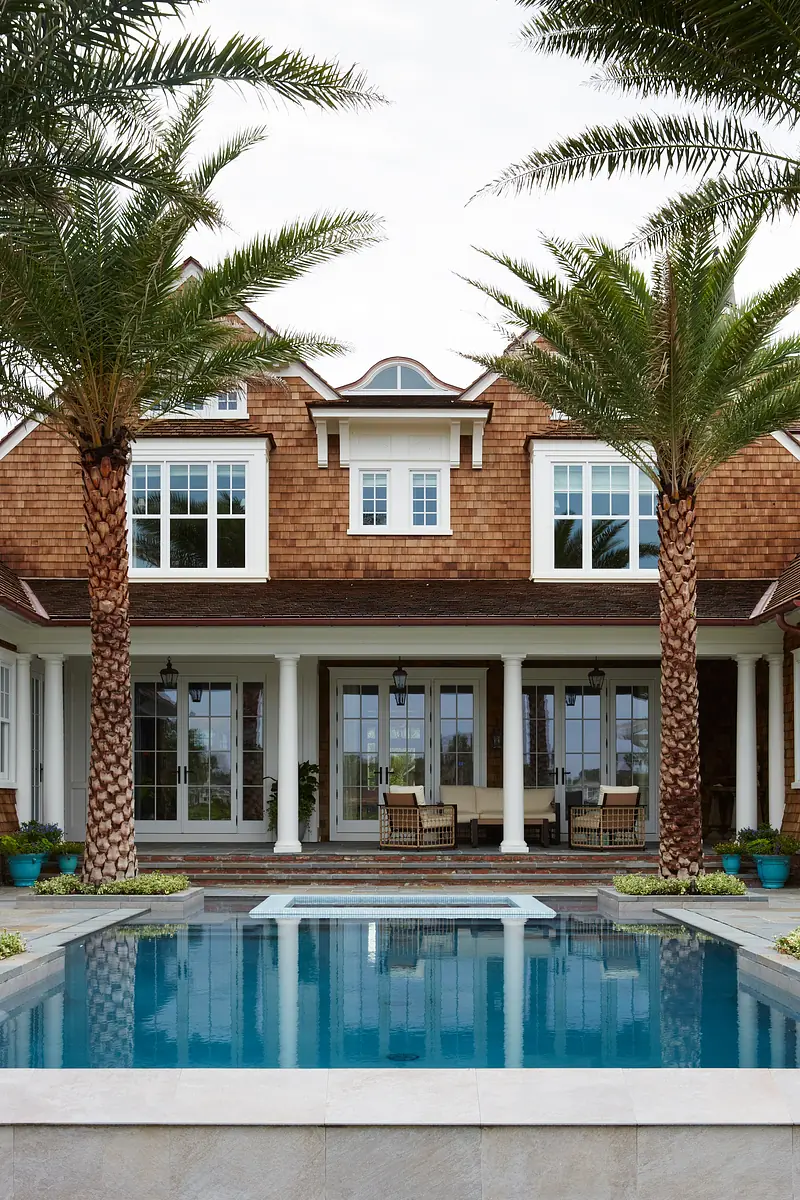 Exterior view of a house with swimming pool, palm trees, and covered porch with wicker chairs.