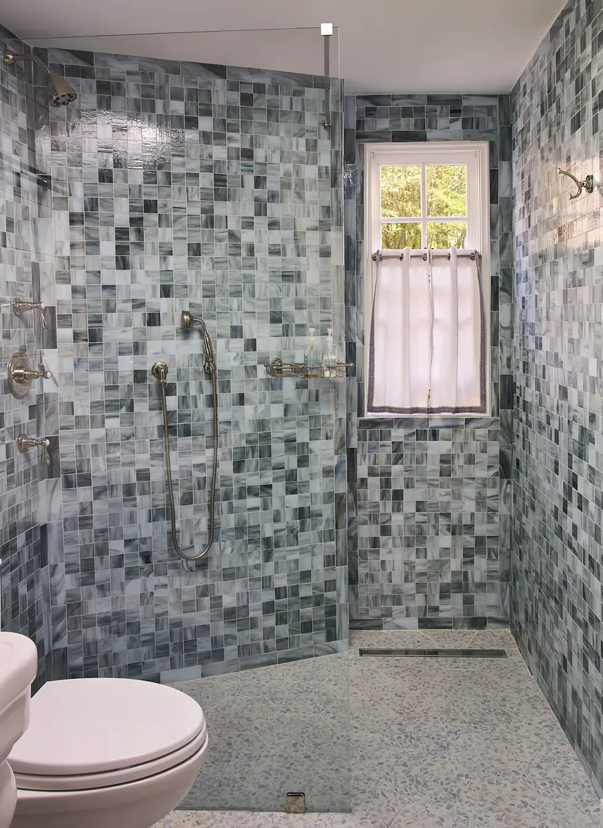 Bathroom with glass shower, mosaic tile walls, white toilet, and a small window.