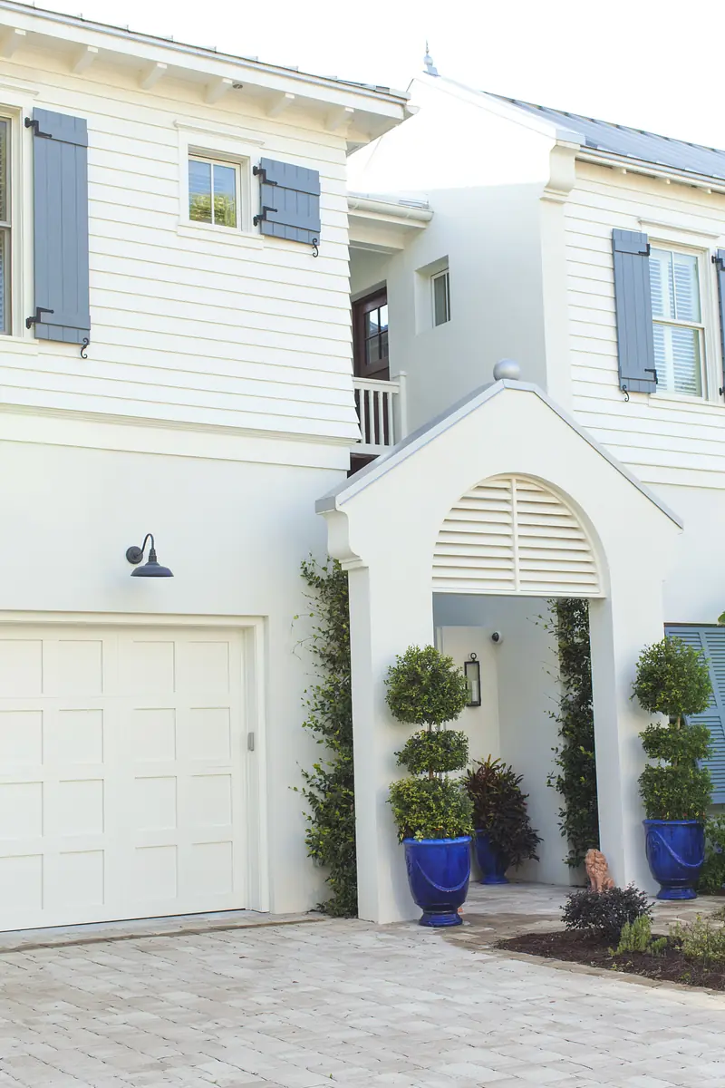 Exterior front view with white house, blue shutters, arched entrance, topiary, and paver pathway.