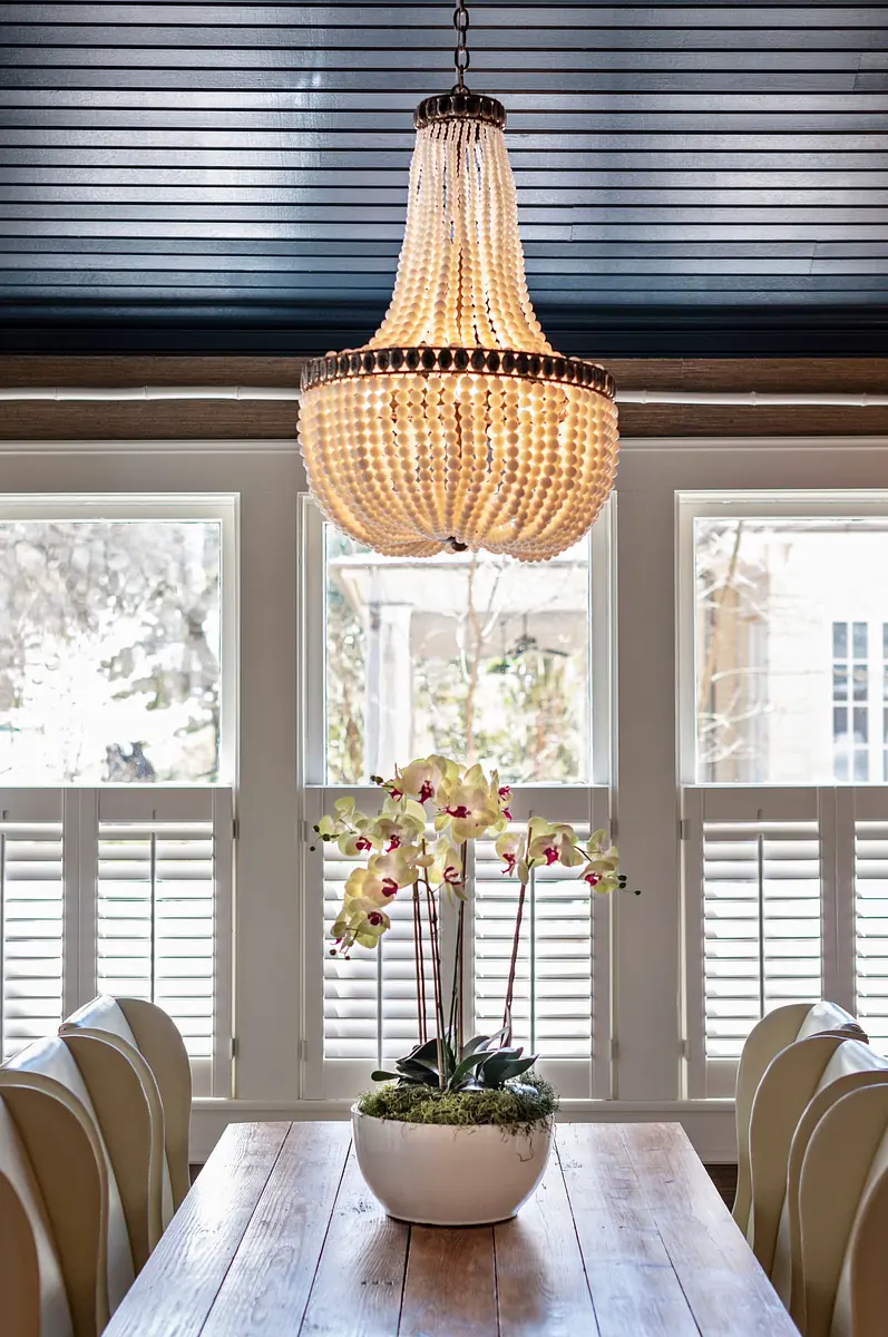 Dining room with wooden table, upholstered chairs, chandelier, and decorative flower arrangement.