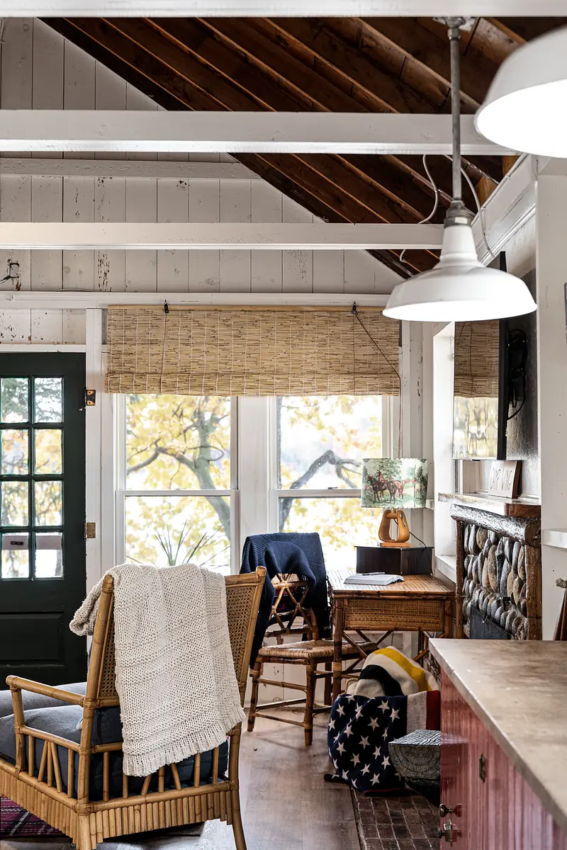 Living room with rattan chair, side table, woven shade window, and exposed beam ceiling.