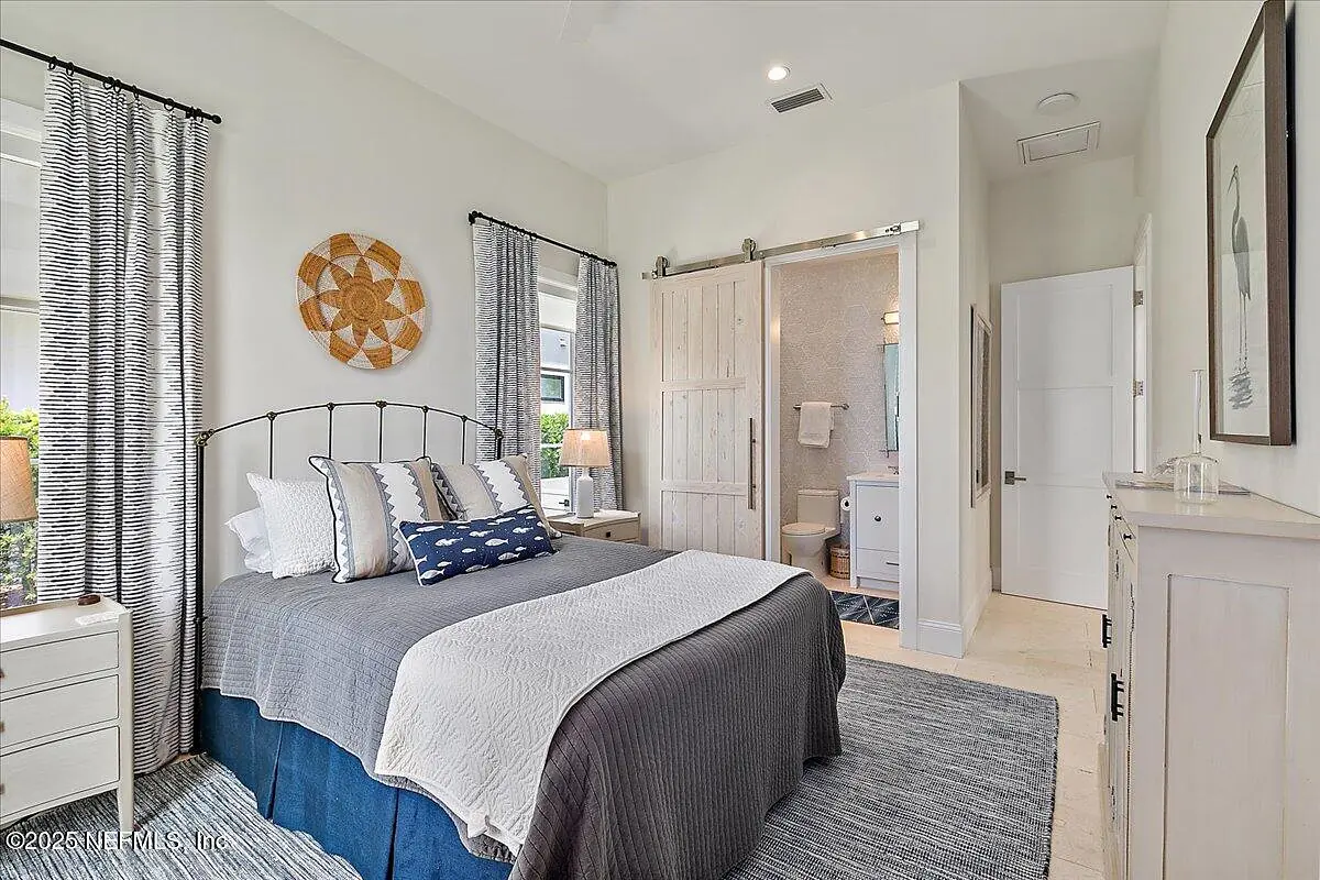 Bedroom with metal bed frame, gray and white bedding, nightstands, lamps, area rug, and access to a bathroom