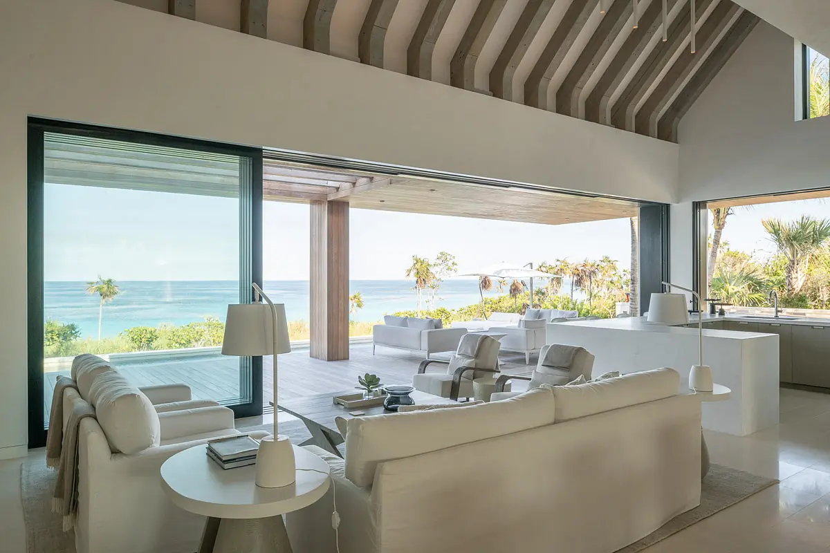 Living room with white sectional sofa, light gray armchairs, side tables, ocean view, and wooden ceiling beams