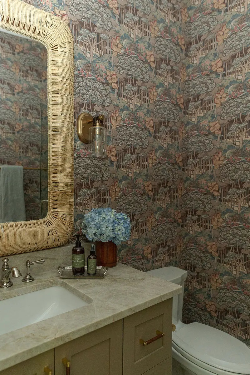 Powder room with beige countertop, dual sinks, floral wallpaper, wooden hydrangea container, and white toilet.