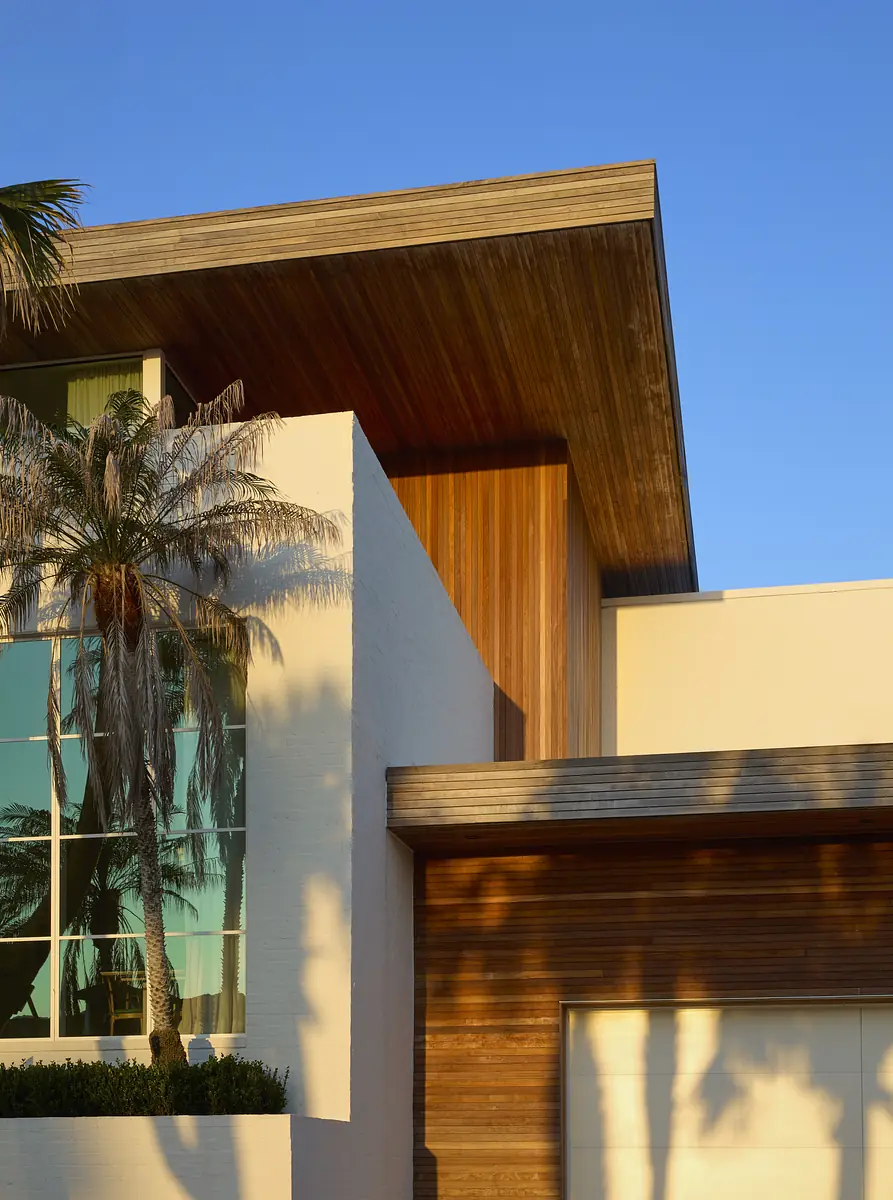 Modern home exterior with flat roof, wooden overhang, glass windows, and palm trees