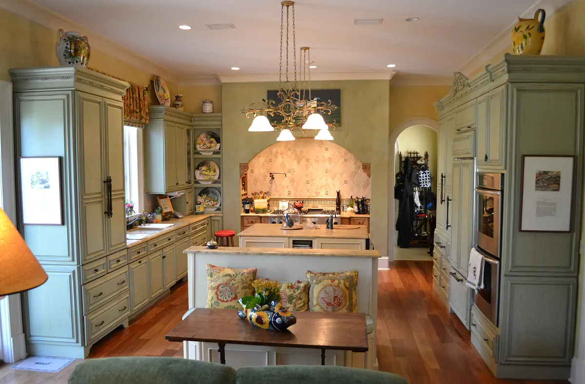 Kitchen with green cabinetry, central island, wooden table, appliances, and decorative wall art